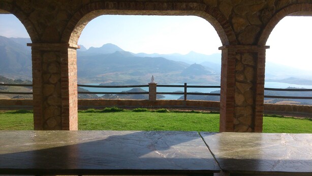 A stone structure with arches, a stone table, and a view of mountains and a lake.