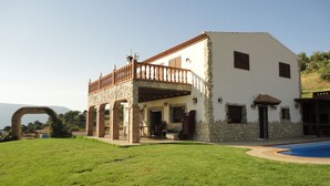 A two-story house with a stone facade, a balcony, and a swimming pool.