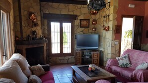 A cozy living room with a stone wall, a fireplace, a television, and comfortable seating.