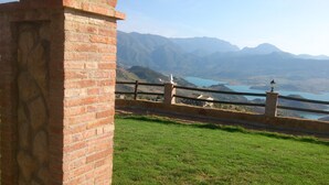 A brick structure with a railing overlooking a mountainous landscape and a body of water.