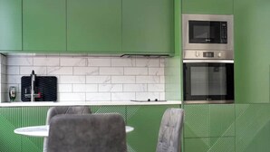 A modern kitchen with green cabinetry, a white countertop, a microwave, and an oven. There is a chair and a table in the foreground. - Lovely Central London Apartment (London)