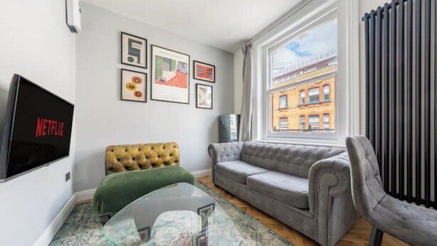 A modern living room with a sofa, a glass coffee table, a green armchair, and a television displaying 'NETFLIX'. - Lovely Central London Apartment (London)