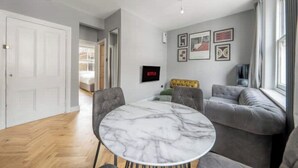 A modern living room with a marble table, grey upholstered seating, and a TV mounted on the wall. - Lovely Central London Apartment (London)