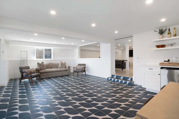 A spacious living area with a patterned floor, a sofa, a chair, and a kitchen area with white cabinets and a countertop.