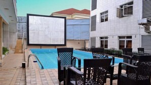 A swimming pool with lounge chairs and a large screen. - Springpark Yaad Hotel (Lagos)