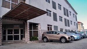 A building with a covered entrance, multiple windows, and a parking area with cars. - Springpark Yaad Hotel (Lagos)