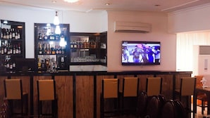 A bar area with a television mounted on the wall displaying a sports event, a bar stocked with various bottles, and several chairs arranged for seating. - Springpark Yaad Hotel (Lagos)