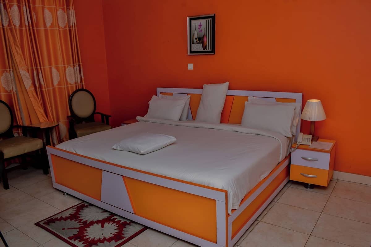 Un dormitorio con cama, mesita de noche, silla y un cuadro en la pared.