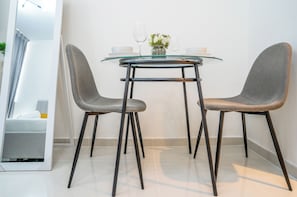 Un espace repas moderne avec une table en verre, deux chaises grises et un vase rempli de fleurs.