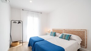 Habitación de hotel con dos camas, un calentador portátil, una mesita de noche con lámpara y una ventana con cortinas.