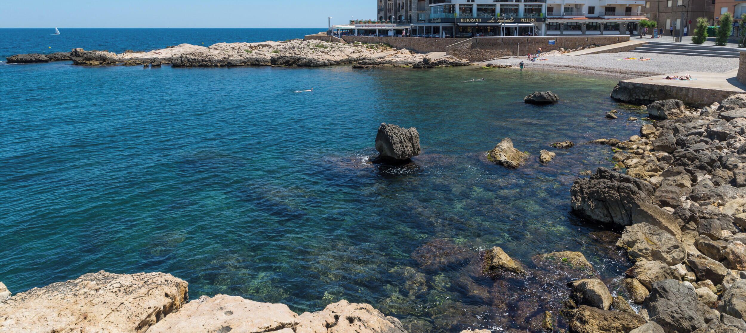 A coastal hotel with clear blue waters, rocky shoreline, and a view of the sea.