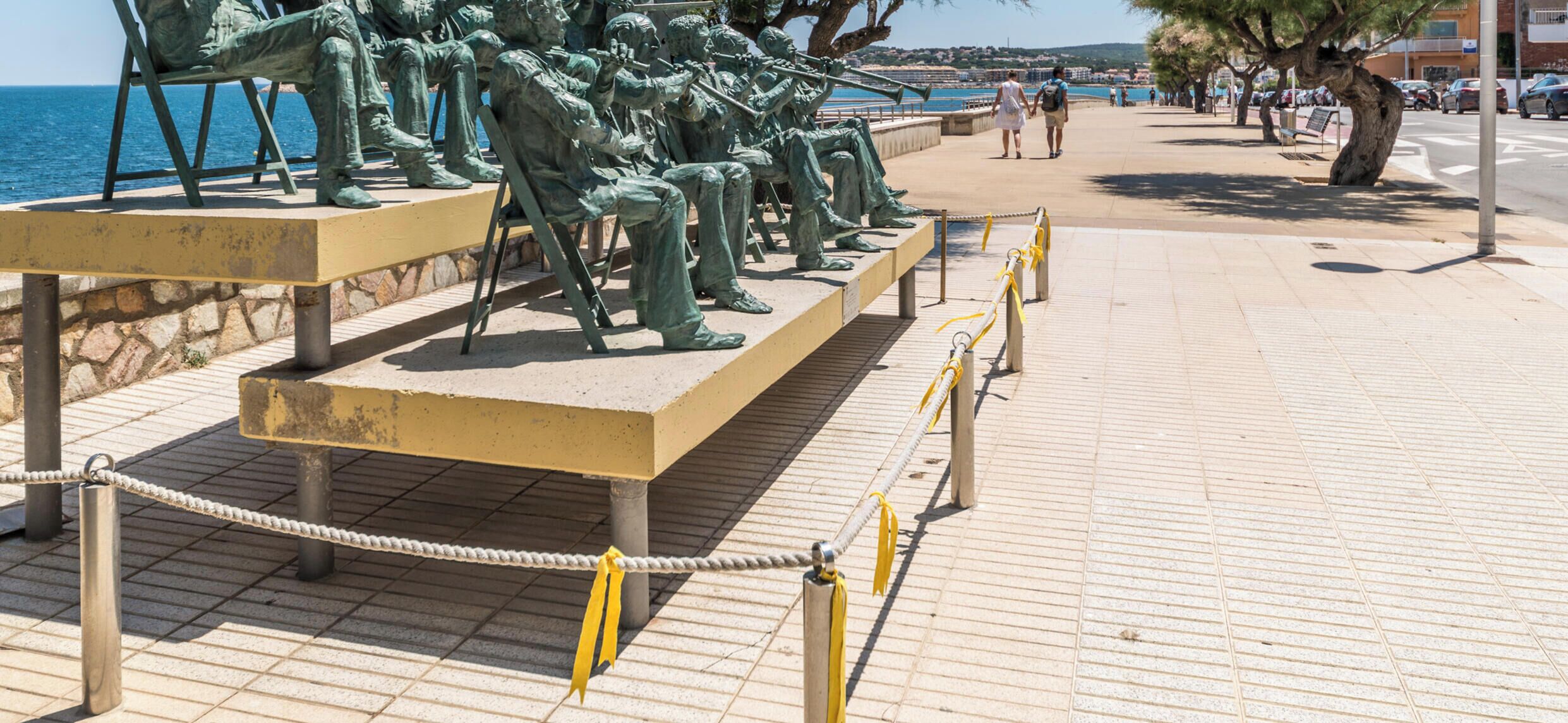 Una estatua de bronce de músicos sentados en un banco junto al mar.