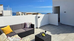 Una terraza en la azotea con un sofá, una mesita y una botella de vino.