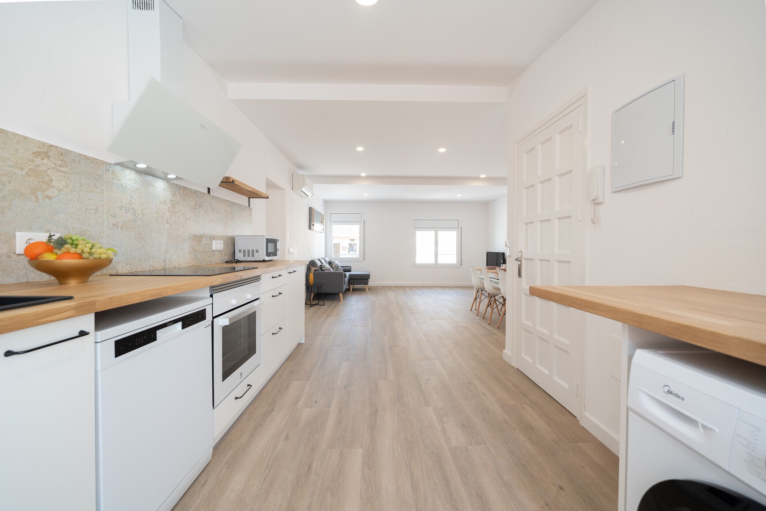 Een moderne keuken met witte apparaten, een houten aanrecht en een eethoek op de achtergrond.