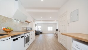 Una cocina moderna con electrodomésticos blancos, encimera de madera y un comedor al fondo.