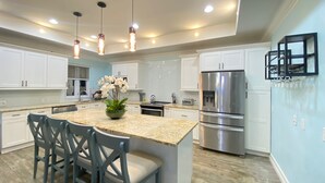 Cocina moderna con armarios blancos, encimera de granito, electrodomésticos de acero inoxidable y una isla central con sillas.