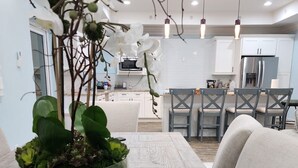 Una cocina moderna con armarios blancos, una zona de comedor con una mesa y sillas de madera, y un tazón verde grande con plantas sobre la mesa.