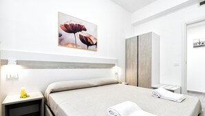 Une chambre d’hôtel avec un lit, une table de chevet avec une lampe, une armoire en bois et un tableau au mur.