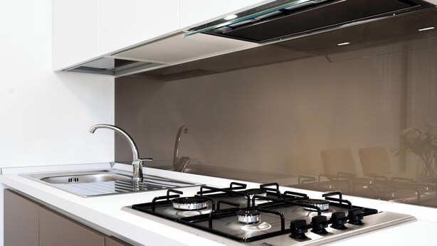 Une cuisine moderne dotée d’une cuisinière à gaz en acier inoxydable, d’un évier et d’un élégant pare-feu.