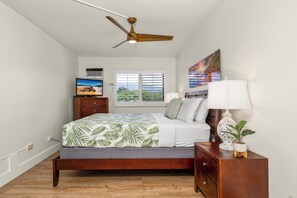 A bedroom with a bed, a nightstand, a ceiling fan, a window with blinds, and a painting on the wall.