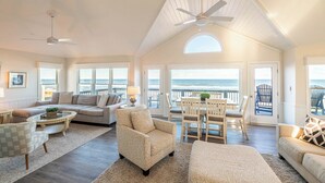 A spacious living room with a large window overlooking the ocean, a ceiling fan, and a cozy seating area with a view.