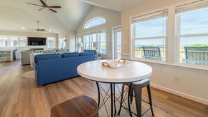 A spacious living area with a blue sofa, a round white table, and a balcony with a view. - Sunrise Dream - Nags Head MP 16, Oceanfront, Ocean View, Pool, Hot Tub, Sauna, Pets OK, Flex Stays (Nags Head)