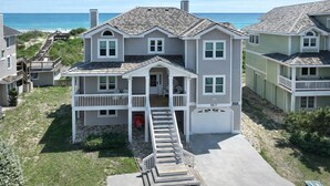 A two-story beachfront house with a balcony, a garage, and a staircase leading to the entrance. - Sunrise Dream - Nags Head MP 16, Oceanfront, Ocean View, Pool, Hot Tub, Sauna, Pets OK, Flex Stays (Nags Head)