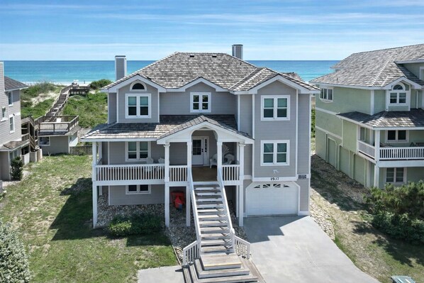 Une maison à deux étages située en bord de mer, dotée d’un balcon, d’un garage et d’un escalier menant à l’entrée.