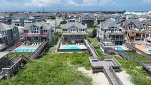 A coastal residential area with multiple two-story houses featuring balconies and swimming pools. - Sunrise Dream - Nags Head MP 16, Oceanfront, Ocean View, Pool, Hot Tub, Sauna, Pets OK, Flex Stays (Nags Head)