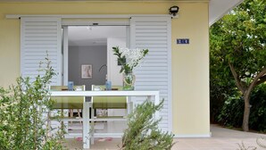 Un espacio de estar al aire libre cubierto, con una mesa, sillas, una planta en maceta y un cartel con la ubicación.