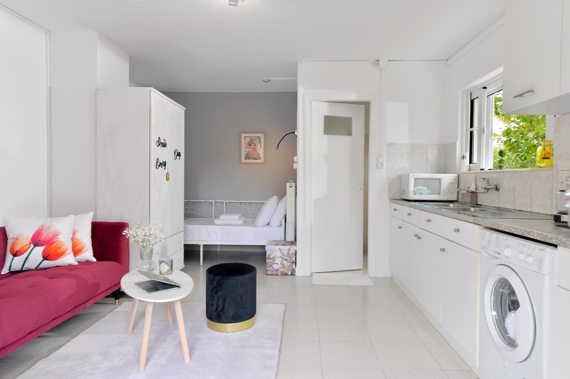 A modern, compact living space with a kitchenette, a bed, and a red sofa.