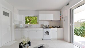 Una cocina moderna con armarios blancos, lavadora, cafetera y un portátil sobre una mesa.