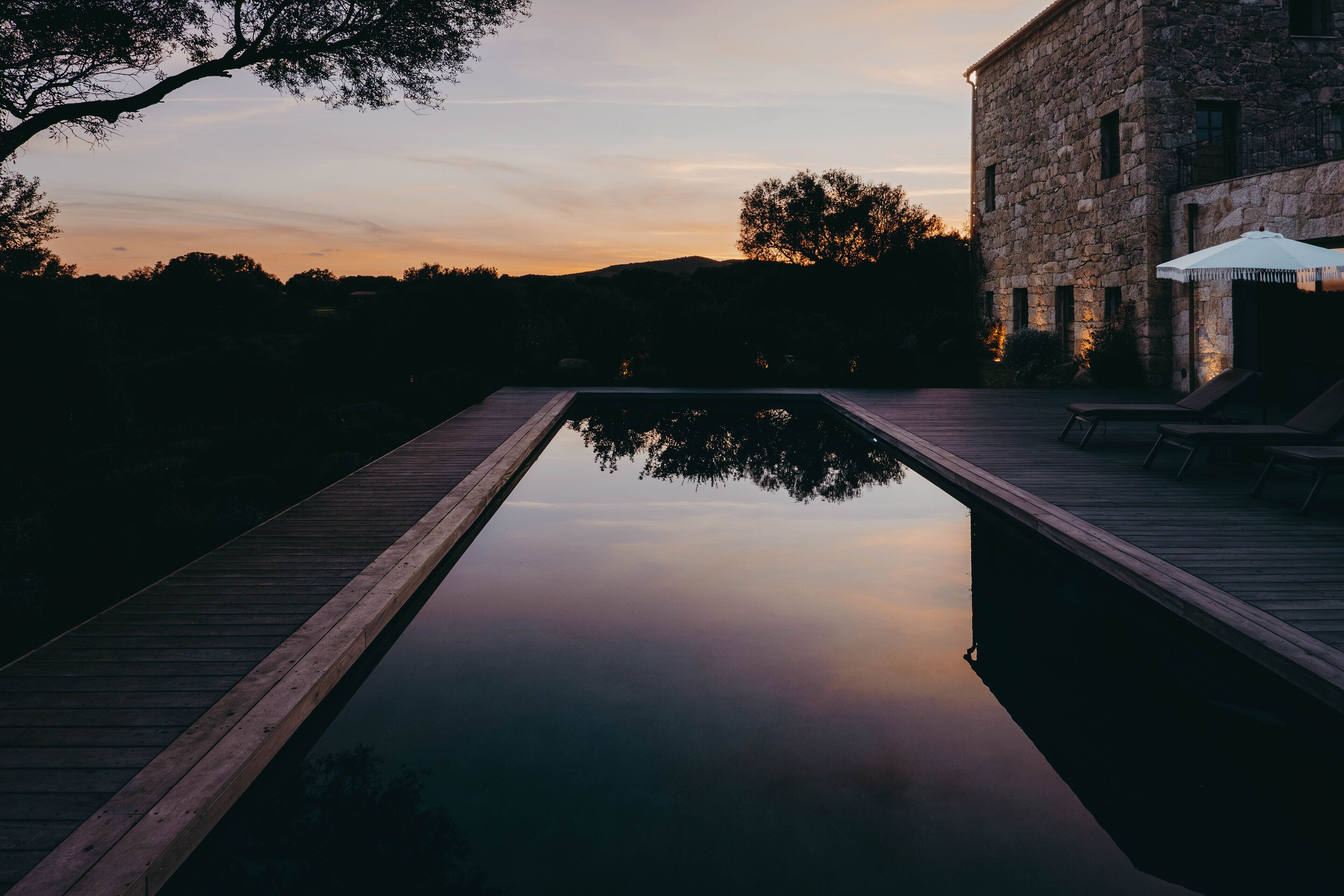 Una piscina amb terrassa de fusta, envoltada d'edificis de pedra, a l'hora del vespre.