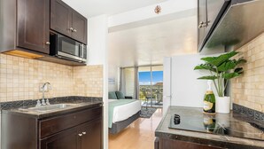 A compact kitchen with a microwave, sink, and a bottle of champagne. - Ocean-Golf Course Couples Retreat at Island Colony Short Walk to the Beach (Honolulu)