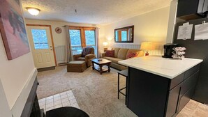 A cozy living room with a sofa, ottoman, and coffee table. There is a kitchen area with a counter and a refrigerator. - Ridgewood 54 - Snowshoe, Short walk to the Powderidge Lift! (Snowshoe)