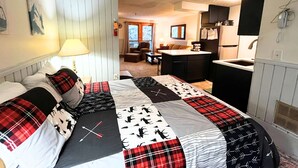 A bedroom with a bed, a nightstand, a lamp, and a view of the living area. - Ridgewood 54 - Snowshoe, Short walk to the Powderidge Lift! (Snowshoe)