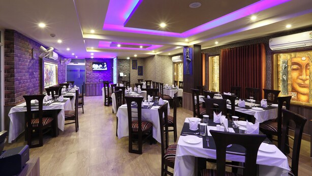 Un restaurant avec plusieurs tables dressées pour le service, un mur de briques d’un côté et une statue de Bouddha accrochée au mur.