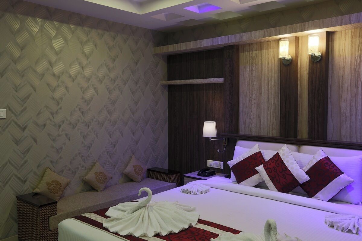Una habitación de hotel con una cama, una mesita de noche, una lámpara y una zona de estar con cojines.