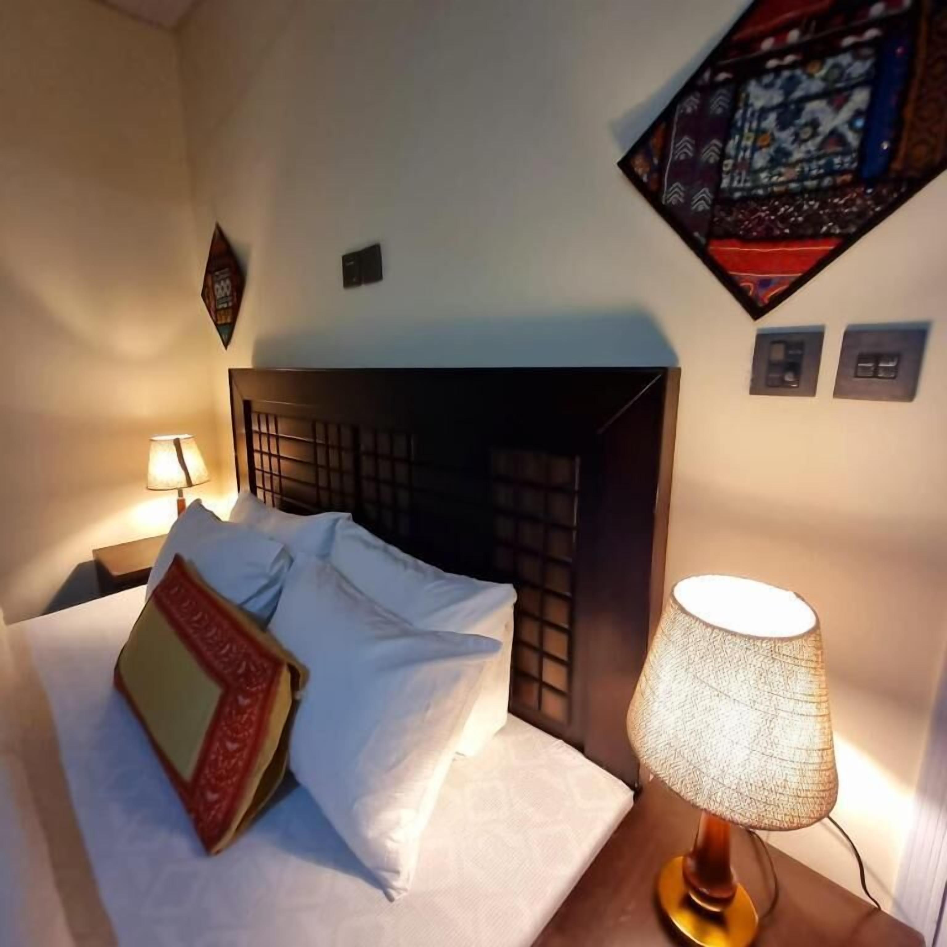 A neatly made bed with white linens and a decorative pillow, a bedside lamp, and a wall-mounted artwork above the bed.