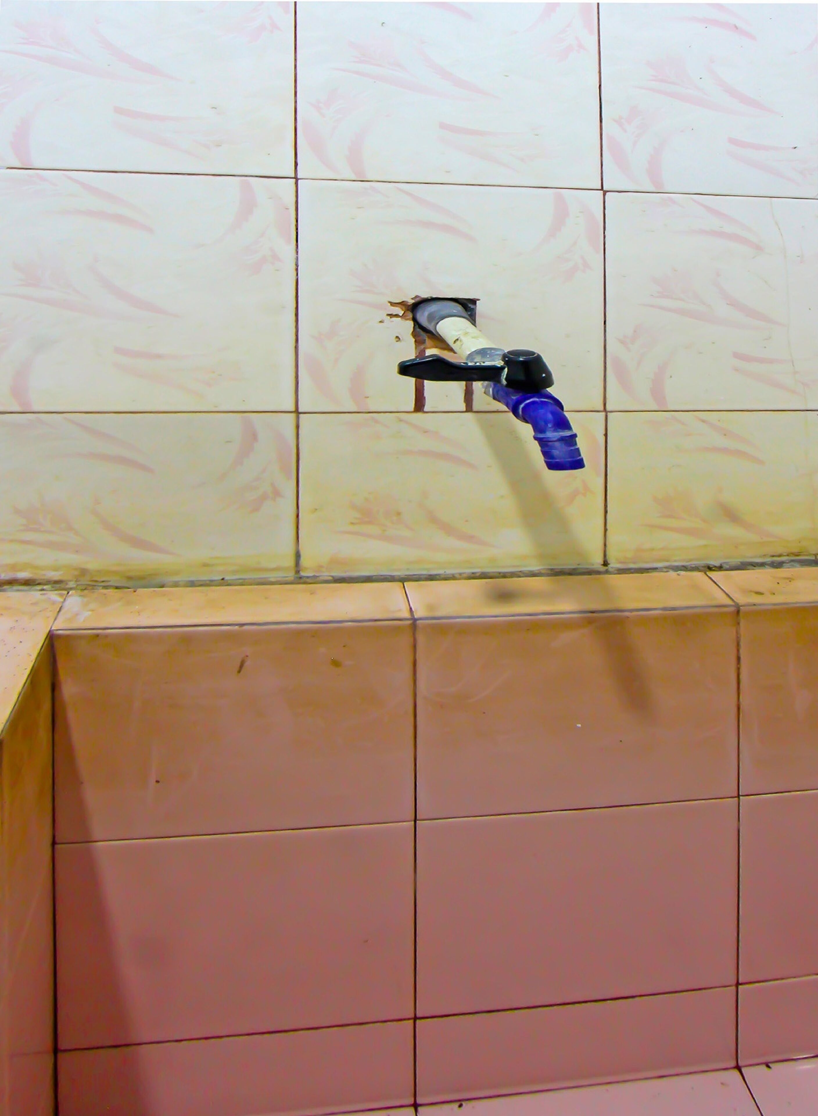 A bathroom with a damaged wall and a blue hand dryer.
