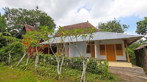 A single-story house with a tiled roof, surrounded by lush greenery and a small garden area. - Hotel O Jati Homestay Near Taman Suranadi (Selong Belanak)