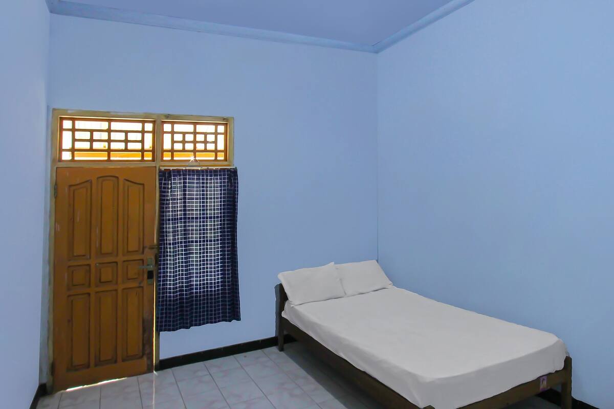A room with a single bed, a wooden door, and a window with a curtain.