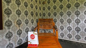 A wooden chair and a table with a sign in front of a wallpapered wall. - Hotel O Jati Homestay Near Taman Suranadi (Selong Belanak)