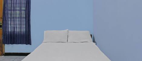 A single bed with white bedding in a room with a blue wall and a checkered curtain.