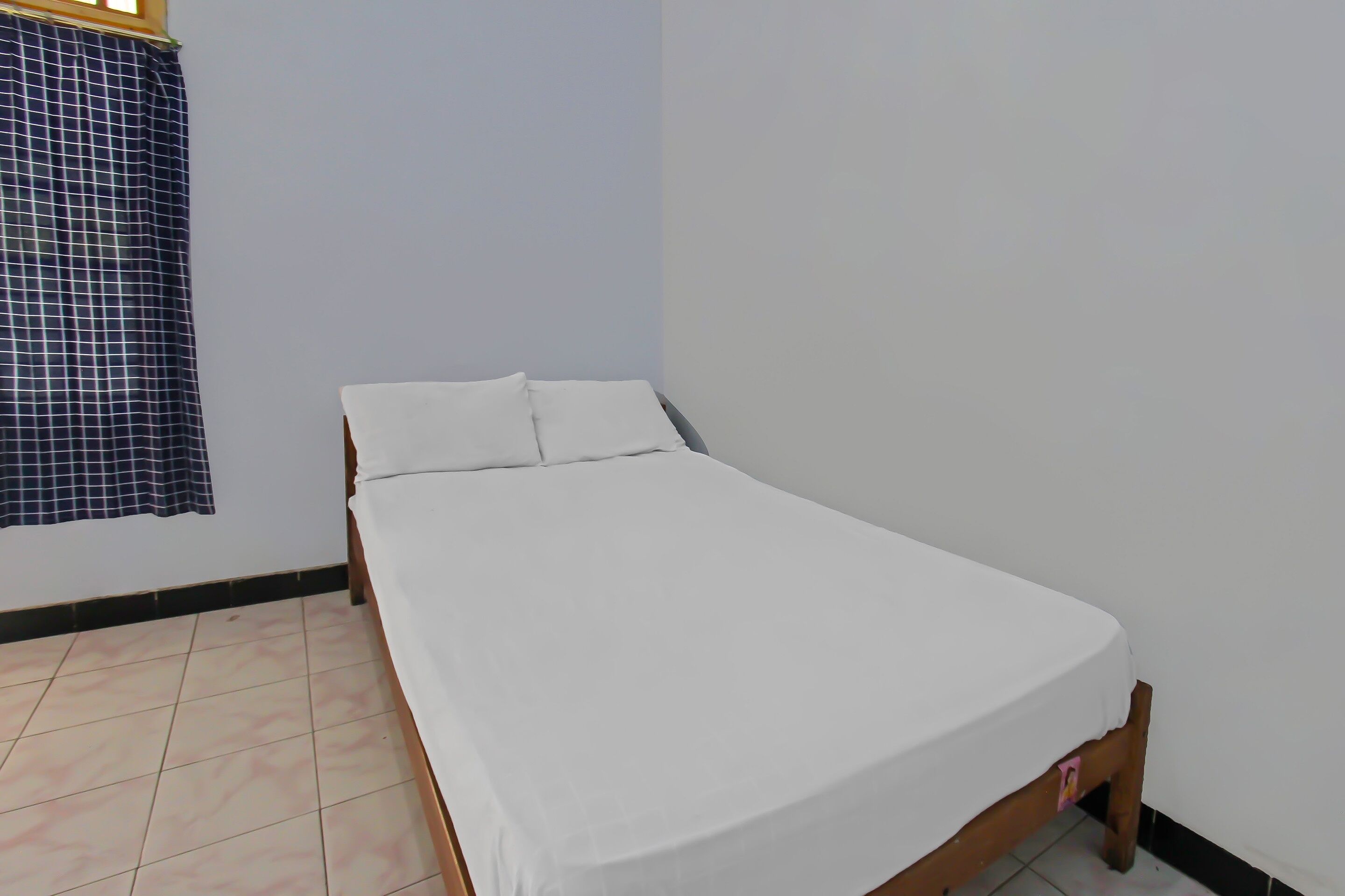 A single bed with white bedding in a room with light blue walls and a checkered curtain.