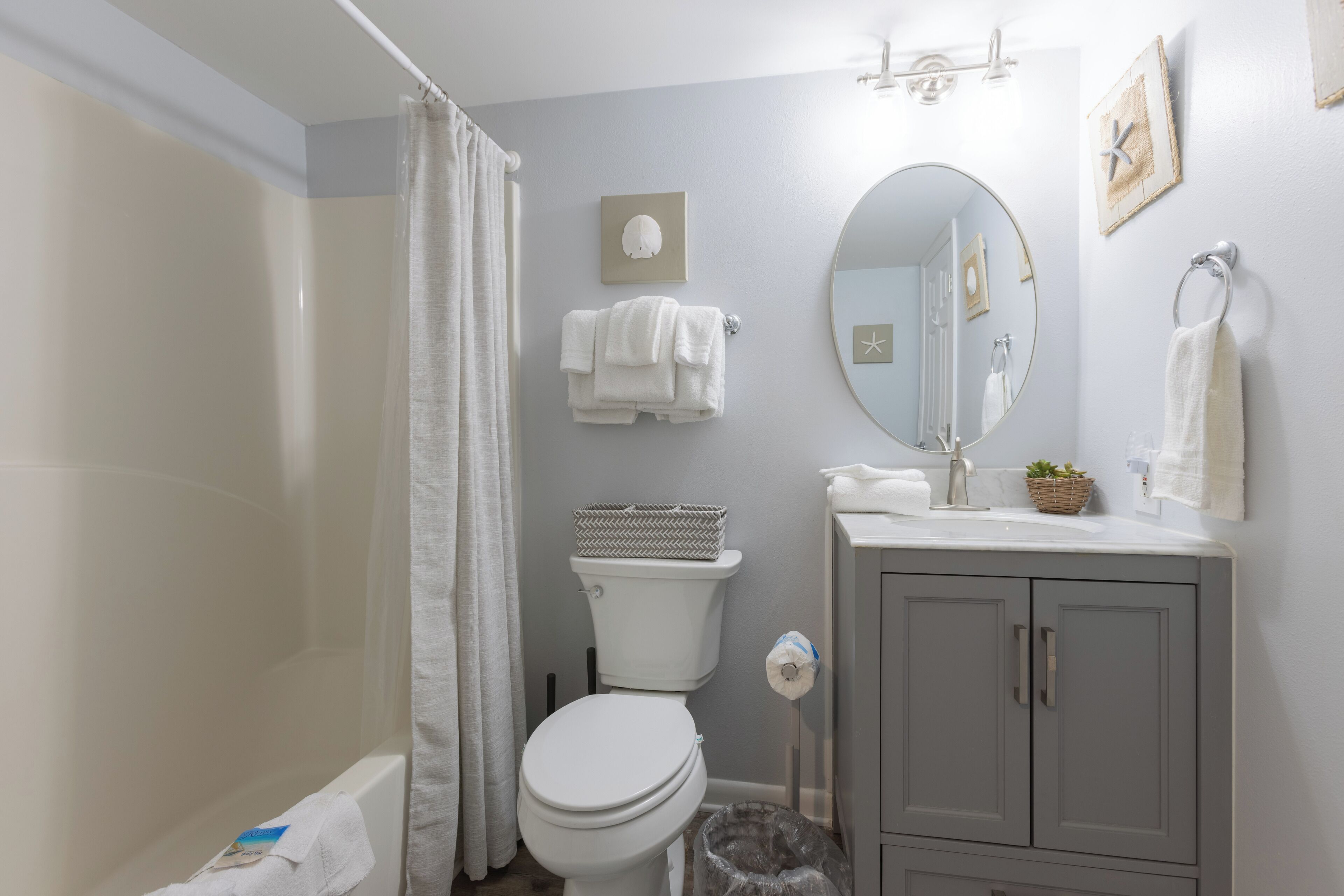 Une salle de bain comprenant des toilettes, un lavabo avec un miroir, un rideau de douche et une poubelle.