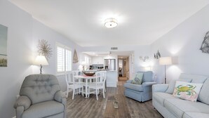 A living room with a grey armchair, a blue sofa, and a dining area with white chairs and a table. - Westwind 204- 5 Star View! Gulf Front! Location X3! Desired Home! (Gulf Shores)