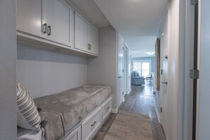 Un couloir étroit avec un lit, une armoire et une porte donnant sur une autre pièce.