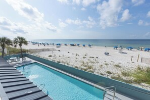 Une piscine située à côté d’une plage, avec des parasols et des chaises longues.
