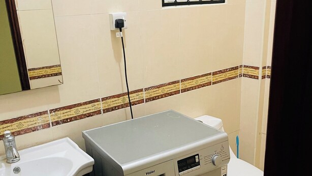 A compact bathroom with a washing machine, a sink, and a toilet. - Near the ocean  with Swimming pool ,Supermarket and ATM machine at the premises. (Dar es Salaam)